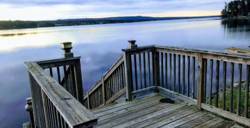 A wooden staircase leads to a calm lake under a cloudy sky with distant trees on the horizon, reminiscent of the tranquility experienced after seamless managed IT services in Northville.