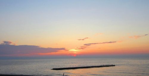 Sunset over a calm sea with a jetty extending into the water and a managed IT services beach in the foreground, serving both Portland and New York.