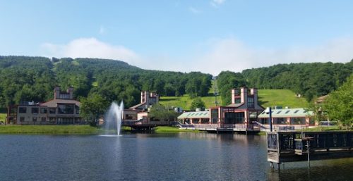 Lakeside resort with managed IT service in Princeton, featuring multiple buildings and a central fountain, set against a green hill under a clear blue sky.
