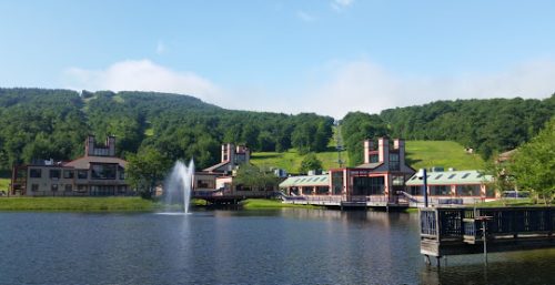 Lakeside resort with managed IT service in Princeton, featuring multiple buildings and a central fountain, set against a green hill under a clear blue sky.