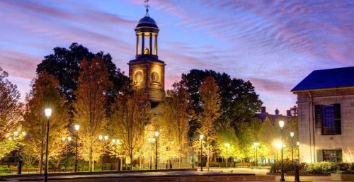 Evening view of a historic bell tower surrounded by illuminated trees on a campus managed IT services Quincy, with wispy clouds in the sky after sunset.