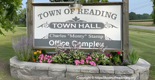 Sign reading "Town of Reading Town Hall Charles 'Monty' Stamp Office Complex" surrounded by flowers and greenery, with a clear sky and a road in the background, showcasing the well-maintained area. Nearby, businesses offer managed IT services to Reading residents.