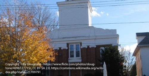 A historical two-story brick building with white architectural details and a prominent tower, surrounded by bare trees, viewed from the street on a clear day in Ripley.