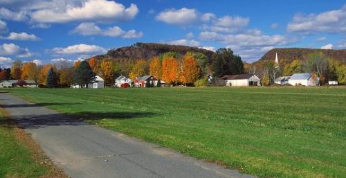 A rural landscape with colorful autumn trees, a few houses managed by an IT service in Sunderland, and a large hill under a partly cloudy sky.
