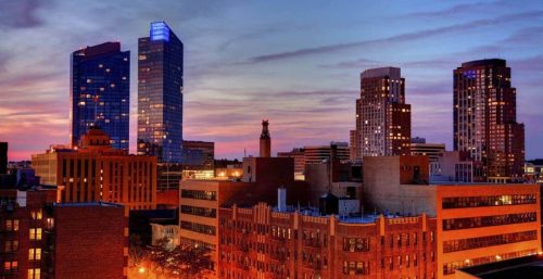 A cityscape at dusk featuring modern and historic buildings under a colorful sky with a mix of orange and purple hues illuminates the vibrant atmosphere of White Plains, where managed IT services expertly blend technology with tradition.