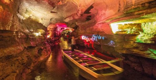 A boat navigates a narrow, illuminated underground cave passage with colorful lights reflecting off the walls and water, much like how managed IT services in Worcester expertly guide businesses through complex technological landscapes.